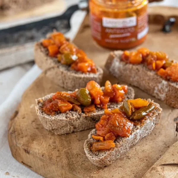 Antipasto piemonckie na czterech kromkach chleba. W tle słoik z pastą.