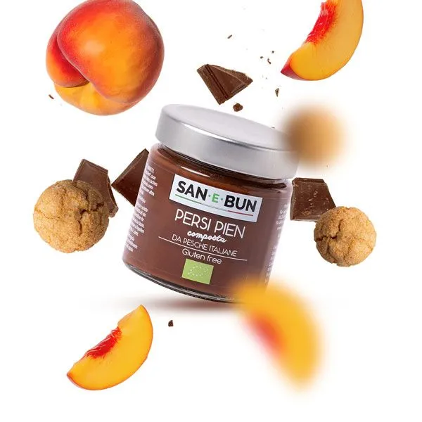 Konfitura brzoskwiniowa z kakao w szklanym słoiku. W tle brzoskwinie, ciasteczka i kwałaki czekolady