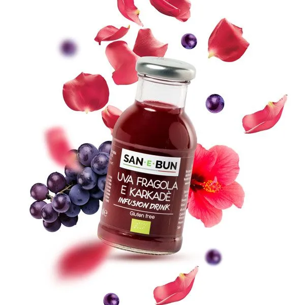 Organiczny napar z hibiskusa, truskawek i winogron w szklanej butelce. W tle winogrona i hibiskus